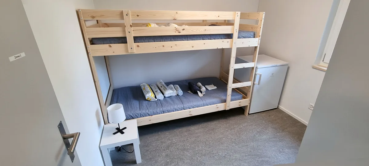 Man sieht ein Schlafzimmer mit einem Hochbett und einem Kühlschrank. 